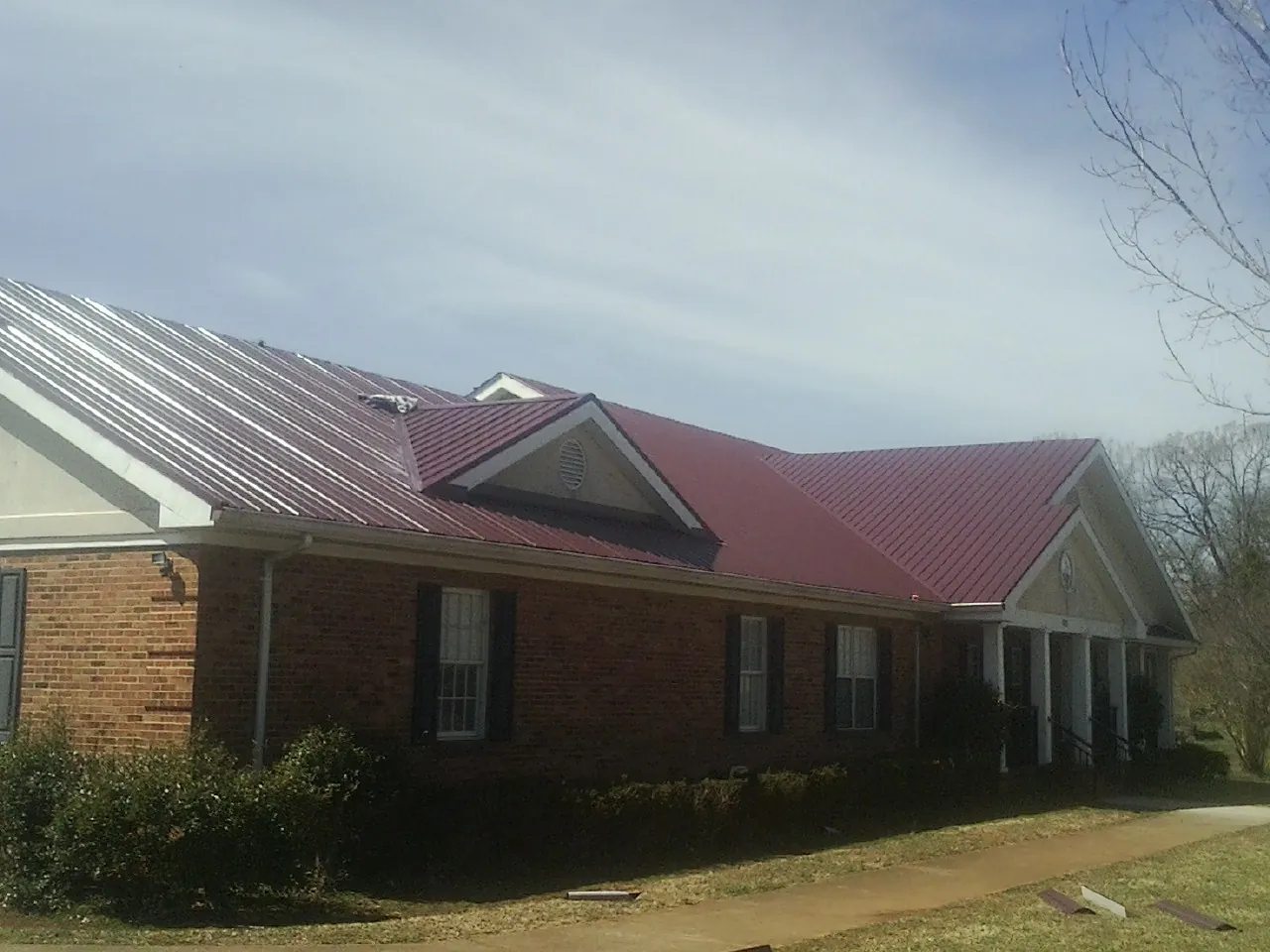 Red metal roof with gabled entries on a long brick building, from a Hail Damage Roof Repair job in Alta Vista