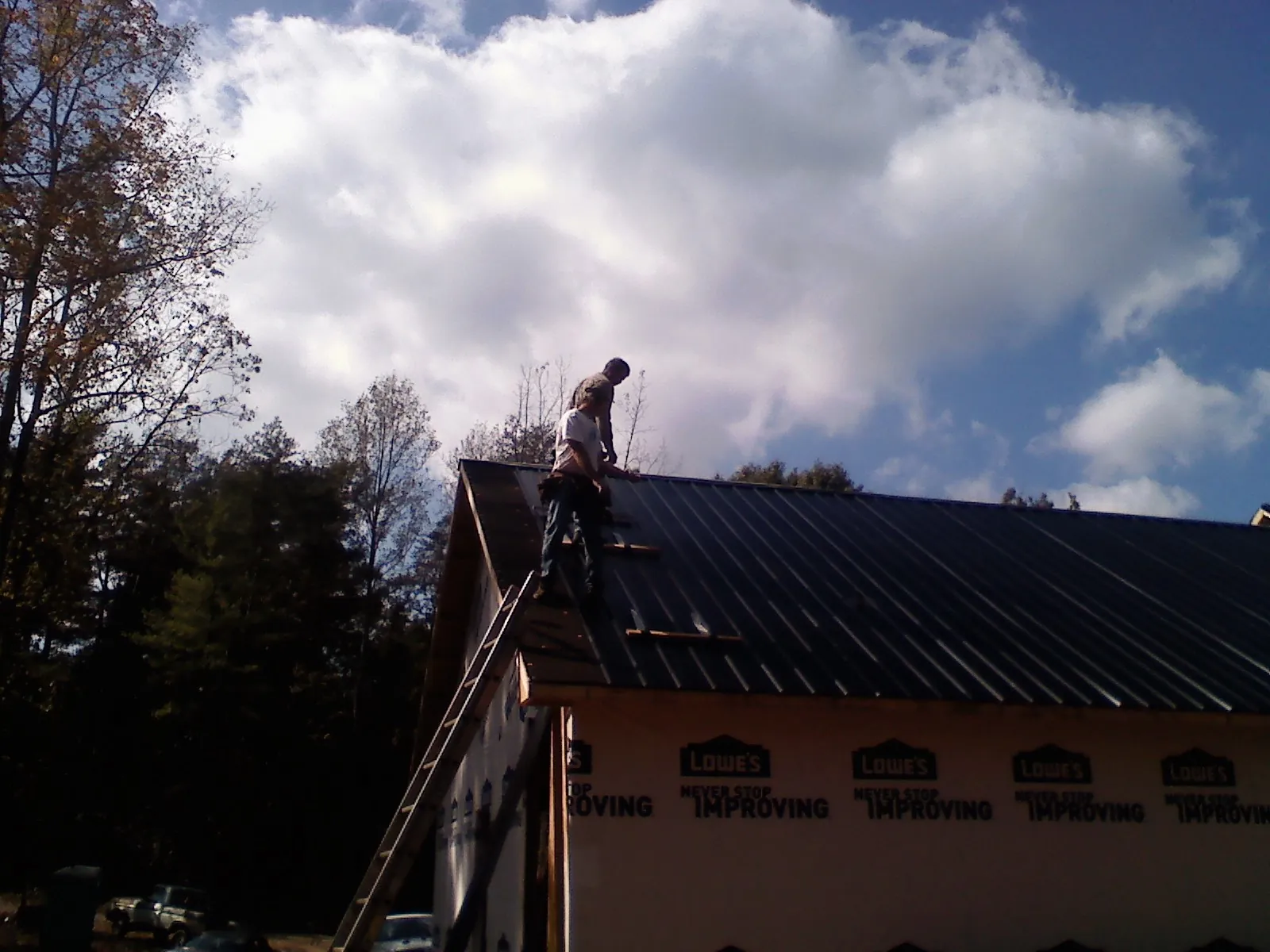 Roofer fastening dark metal panels high against a cloudy sky, from a Roof Inspection job in Alta Vista