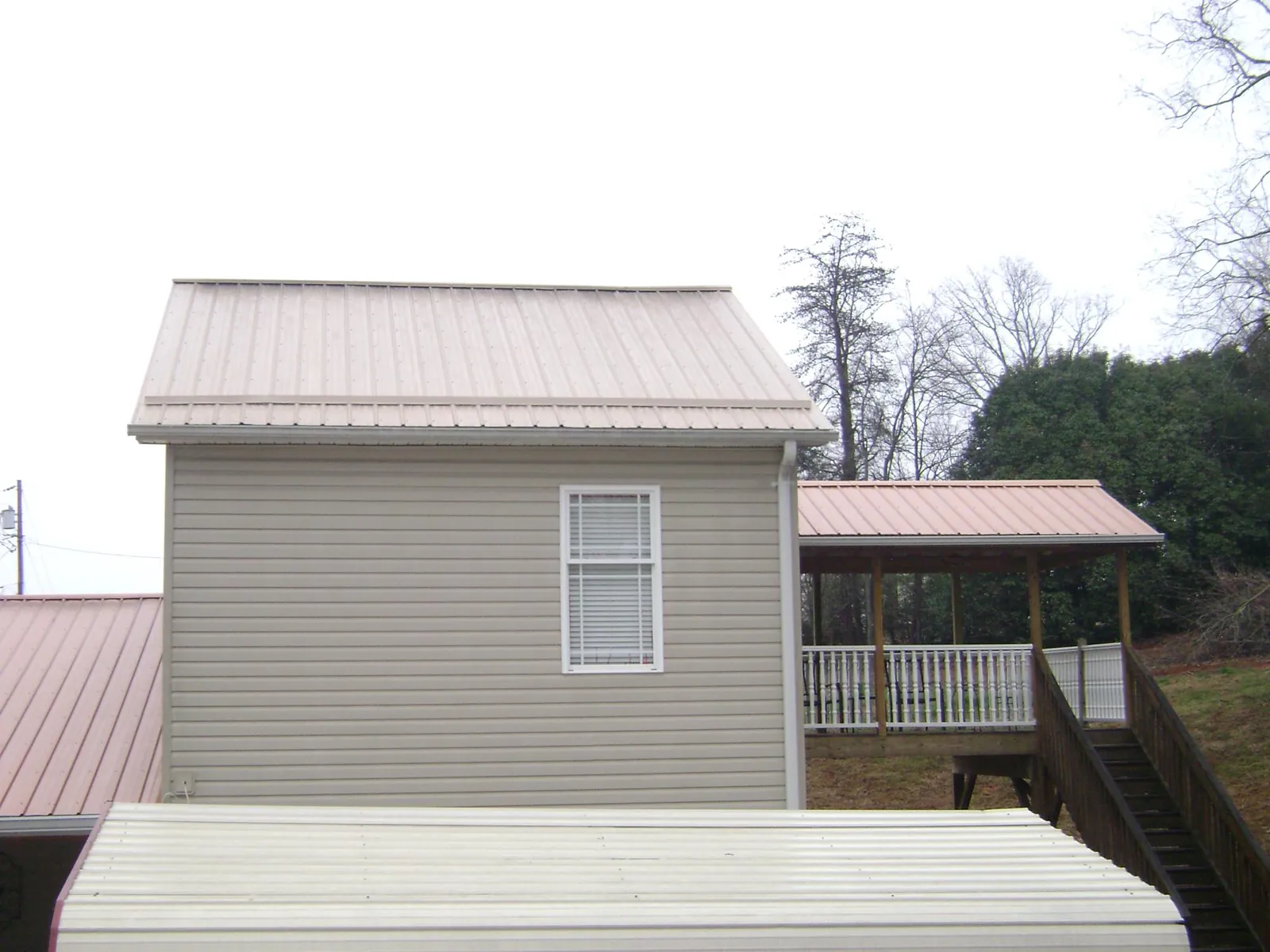 Tan metal roofs on a two story addition and attached porch, from a Roof Replacement job in Alta Vista