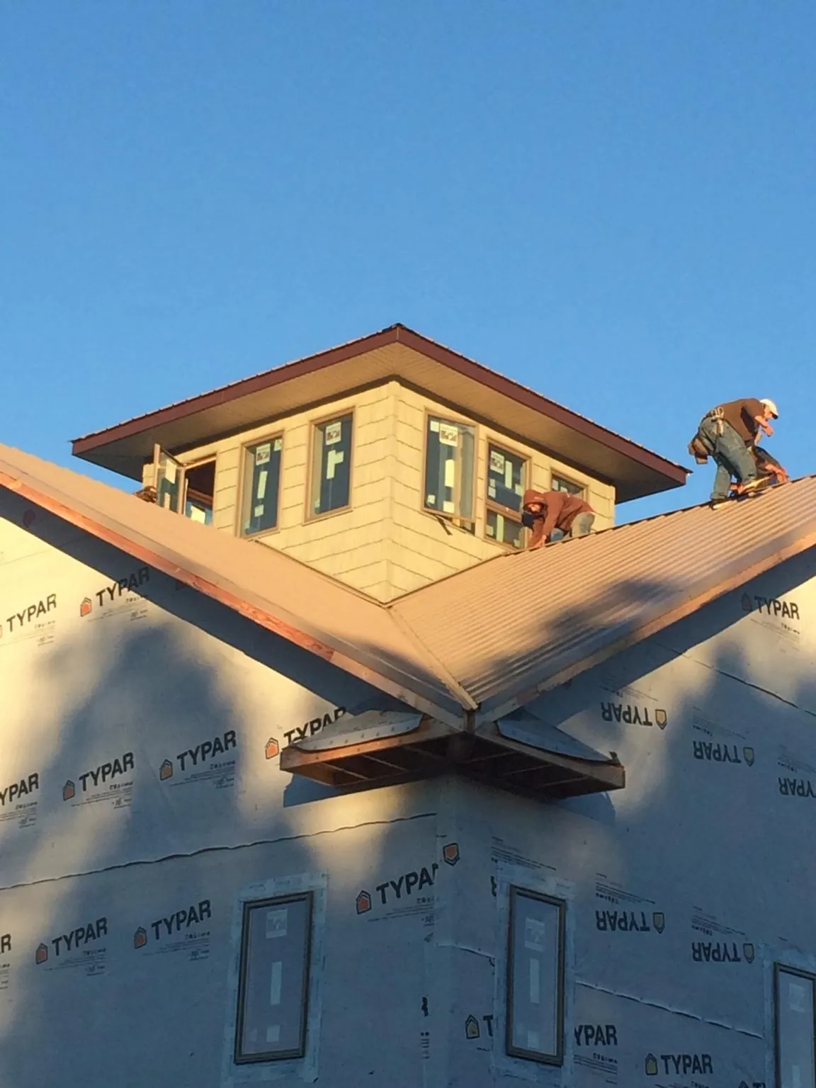 Roofers working around a rooftop cupola on a new metal roof at sunset in Alta Vista